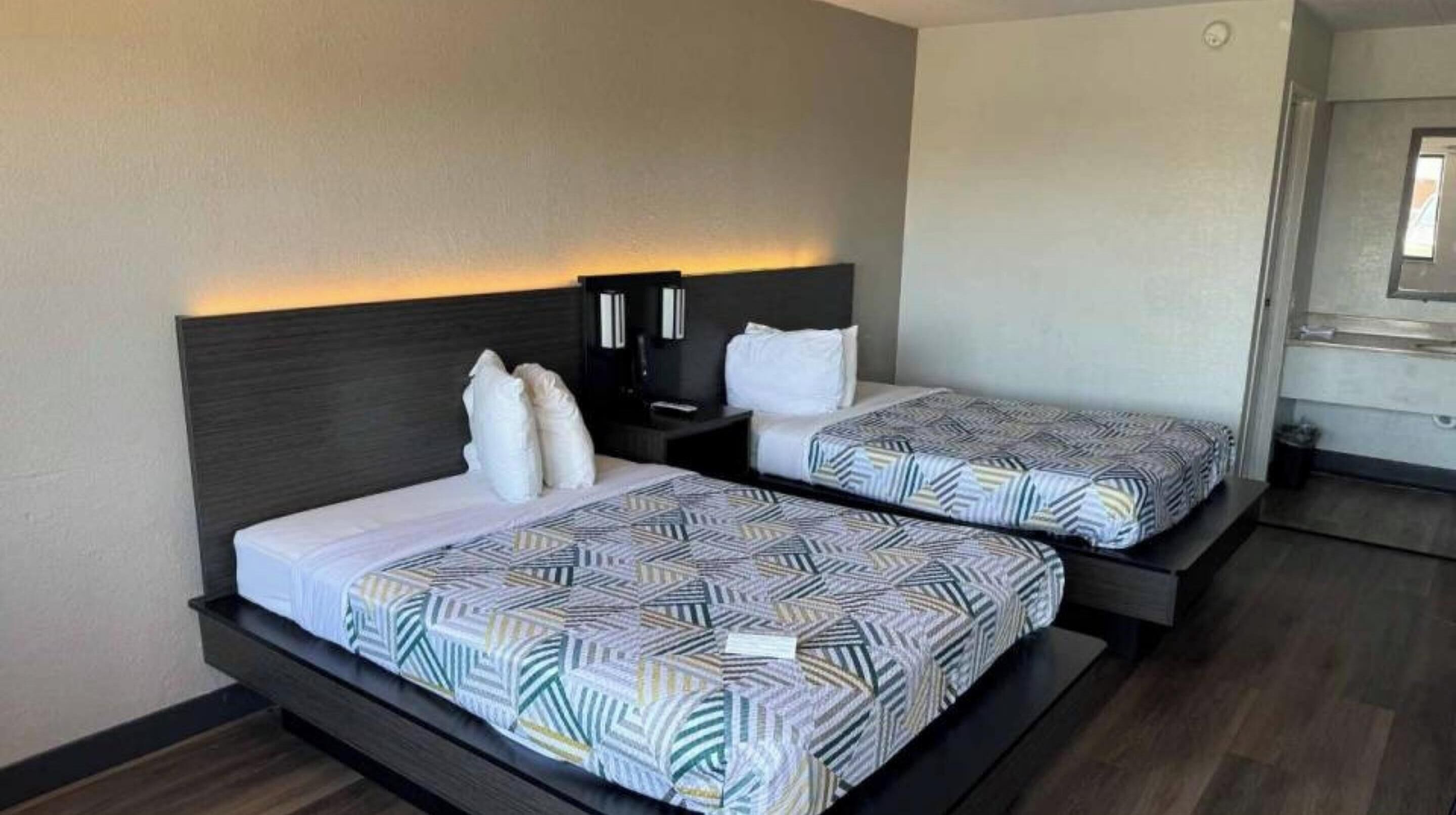 Ein Hotelzimmer mit zwei Betten, jeweils mit einem gemusterten Überwurf, einem dunklen Kopfteil und Nachttischen mit Lampen.