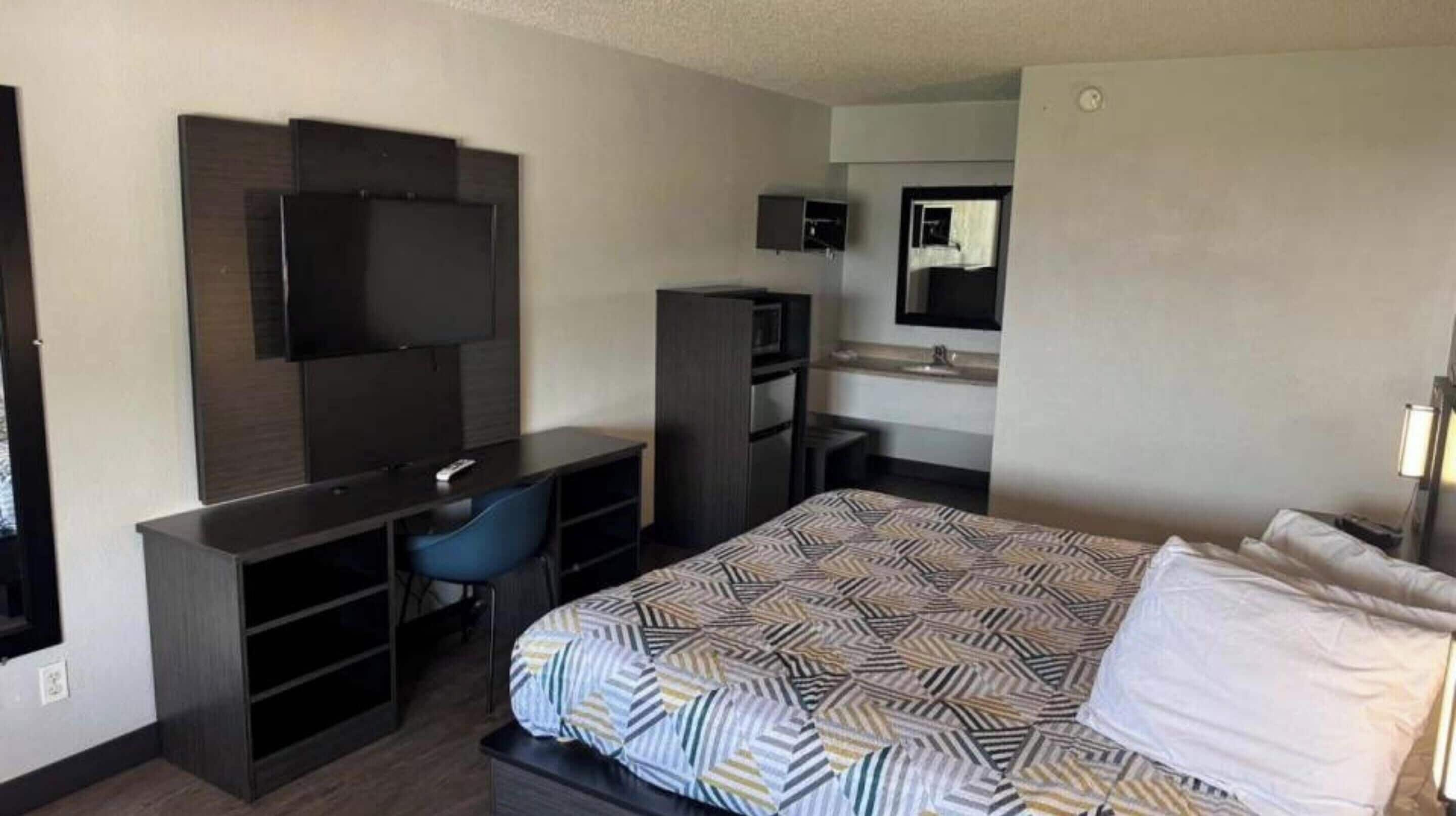 Een hotelkamer met een bed, een bureau met stoel, een televisie, een spiegel en een kitchenette.