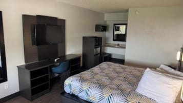 Een hotelkamer met een bed, een bureau met stoel, een televisie, een spiegel en een kitchenette.