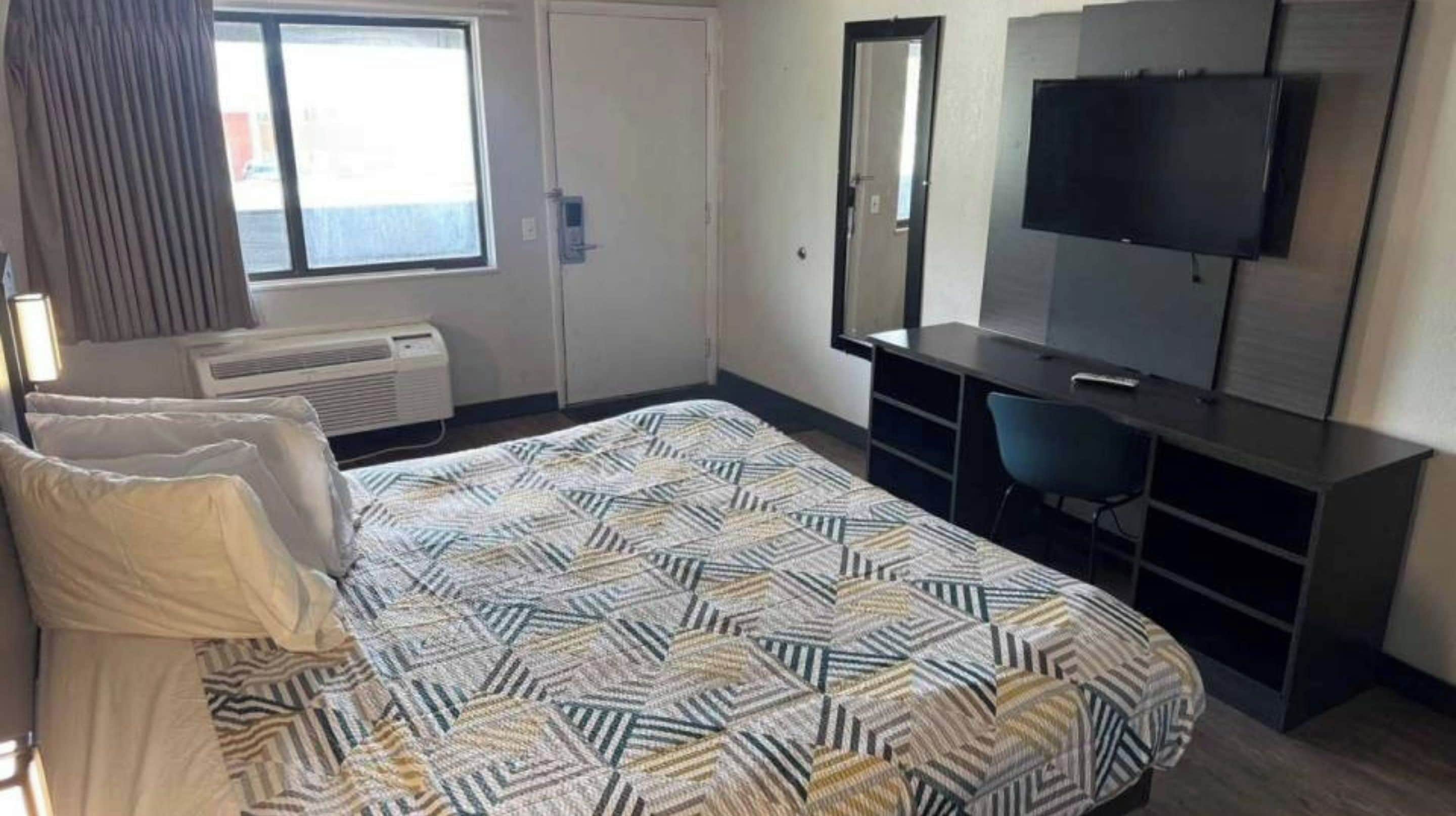 A hotel room with a bed, a desk, a TV, and a window.