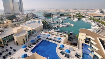Um hotel com piscina no terraço, uma marina com barcos e vista para a costa.