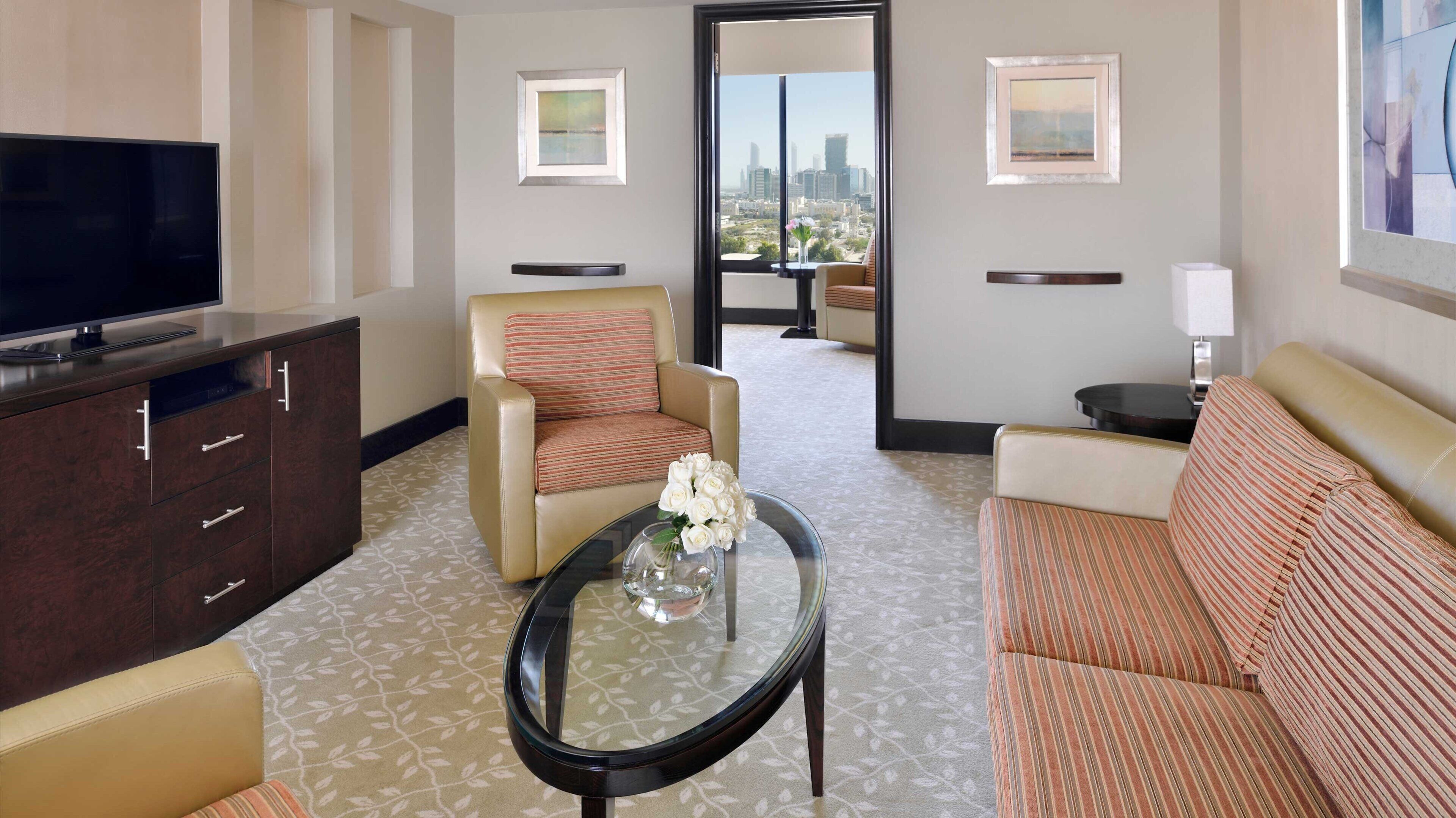 Ein Hotelzimmer mit Fernseher, einer Couch, einem Sessel, einem Couchtisch und Blick auf die Stadt.