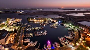 A marina with boats docked, a bridge in the background, and a well-lit waterfront area.