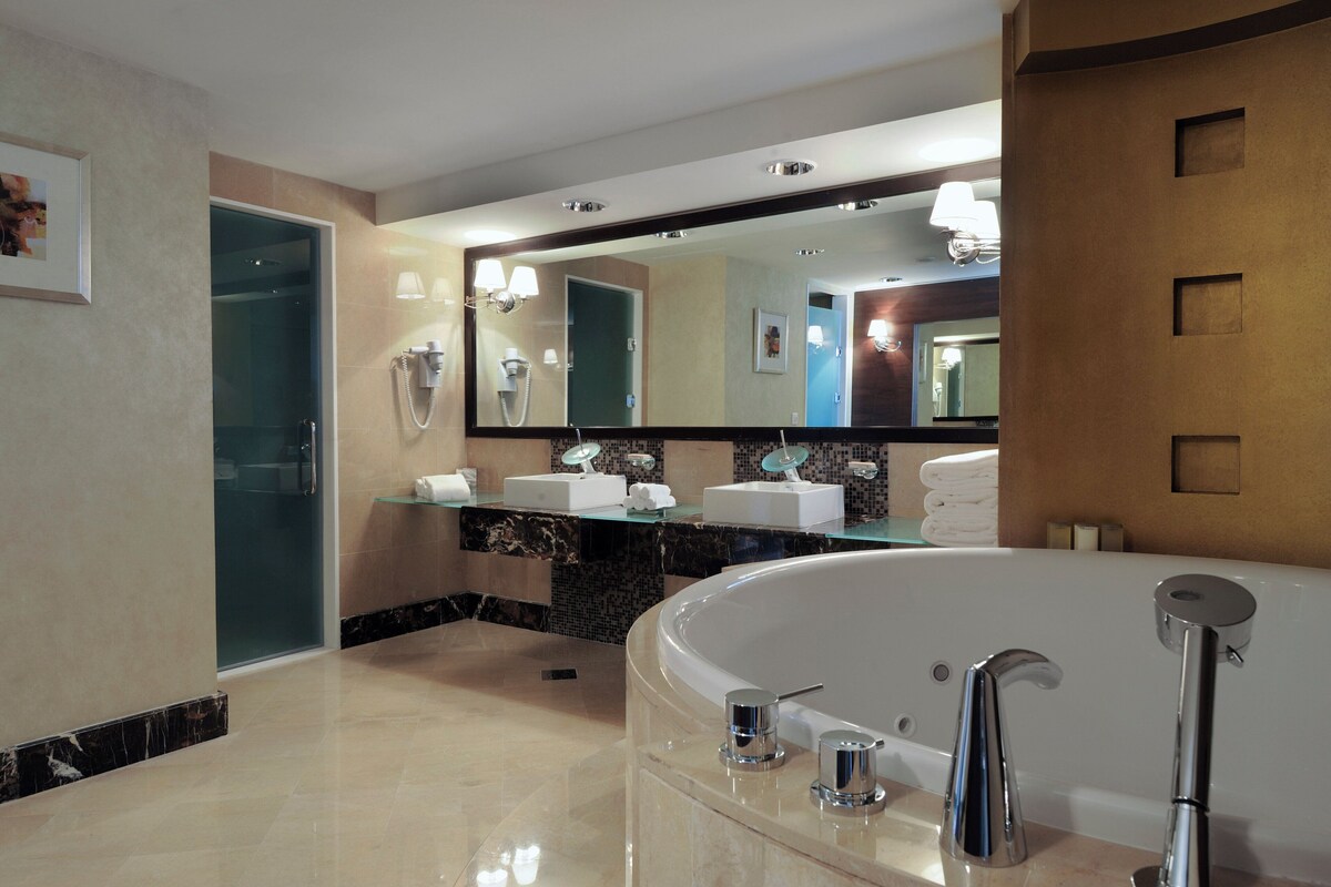 A modern bathroom with a large bathtub, two sinks, a glass shower enclosure, and a large mirror.
