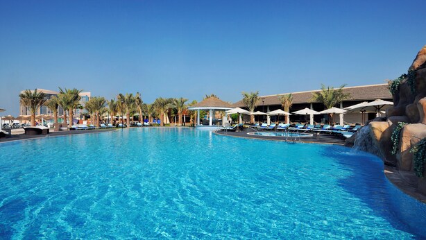 A large, clear blue pool with lounge chairs and umbrellas, surrounded by palm trees and a building in the background. - InterContinental Abu Dhabi by IHG (Abu Dhabi)