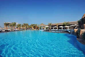 A large, clear blue pool with lounge chairs and umbrellas, surrounded by palm trees and a building in the background. - InterContinental Abu Dhabi by IHG (Abu Dhabi)