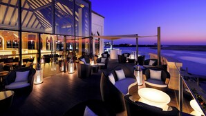 A rooftop bar with outdoor seating, a view of the beach, and a modern building with large windows. - InterContinental Abu Dhabi by IHG (Abu Dhabi)