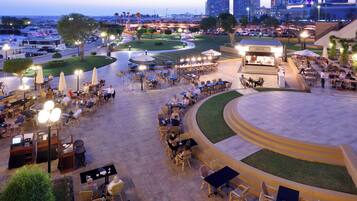 An outdoor dining area with multiple tables and chairs, surrounded by greenery and a curved pathway.