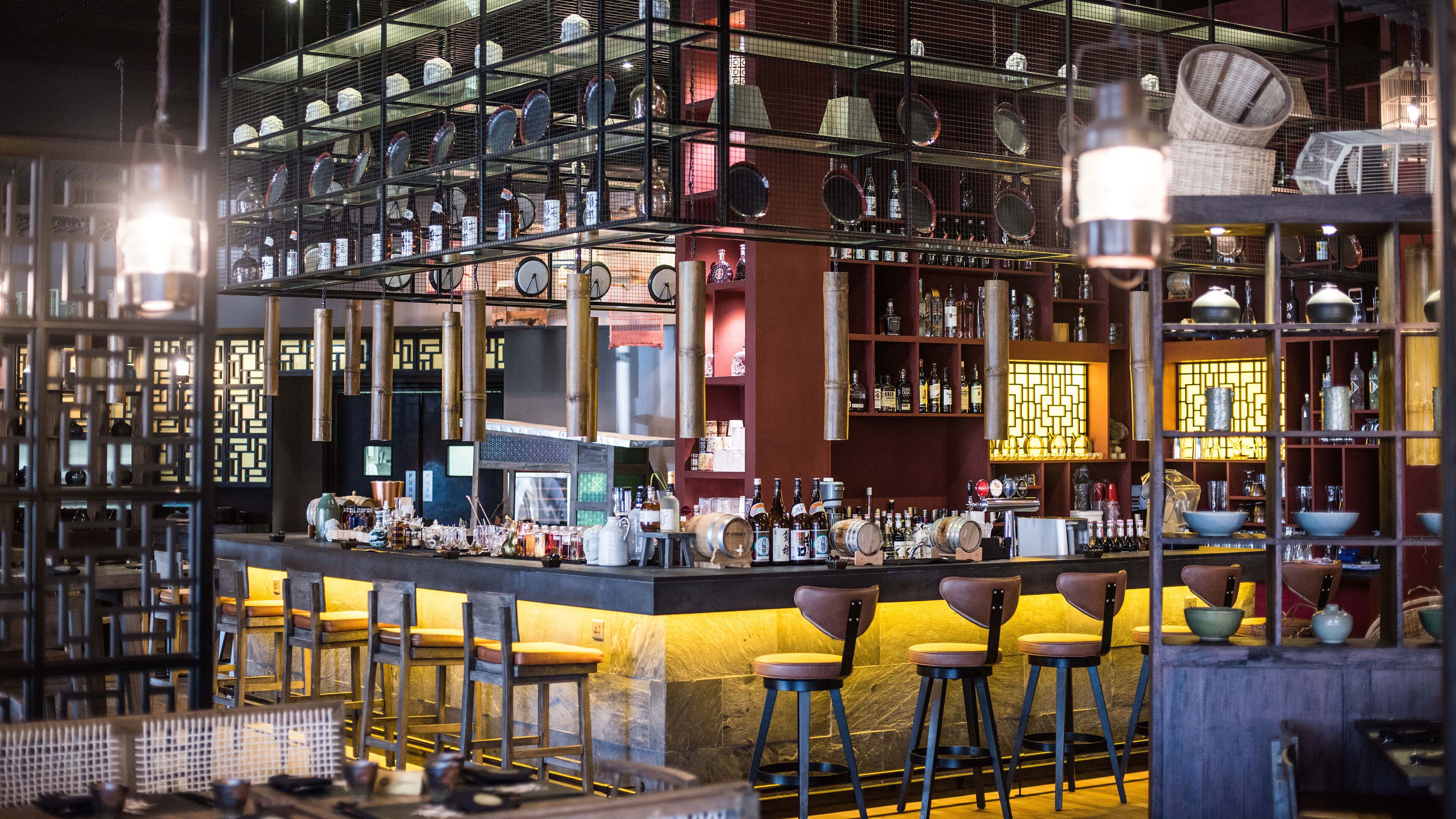 A bar with multiple stools, shelves with bottles, and a variety of barware.