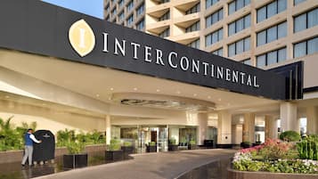 Entrada de hotel com uma grande placa com a inscrição 'INTERCONTINENTAL' e uma área coberta, onde uma pessoa empurra um carrinho.