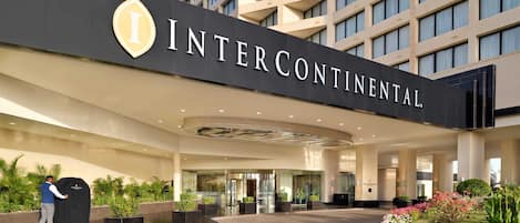 Entrada de un hotel con un cartel grande que dice 'INTERCONTINENTAL' y un área cubierta donde una persona empuja un carrito.