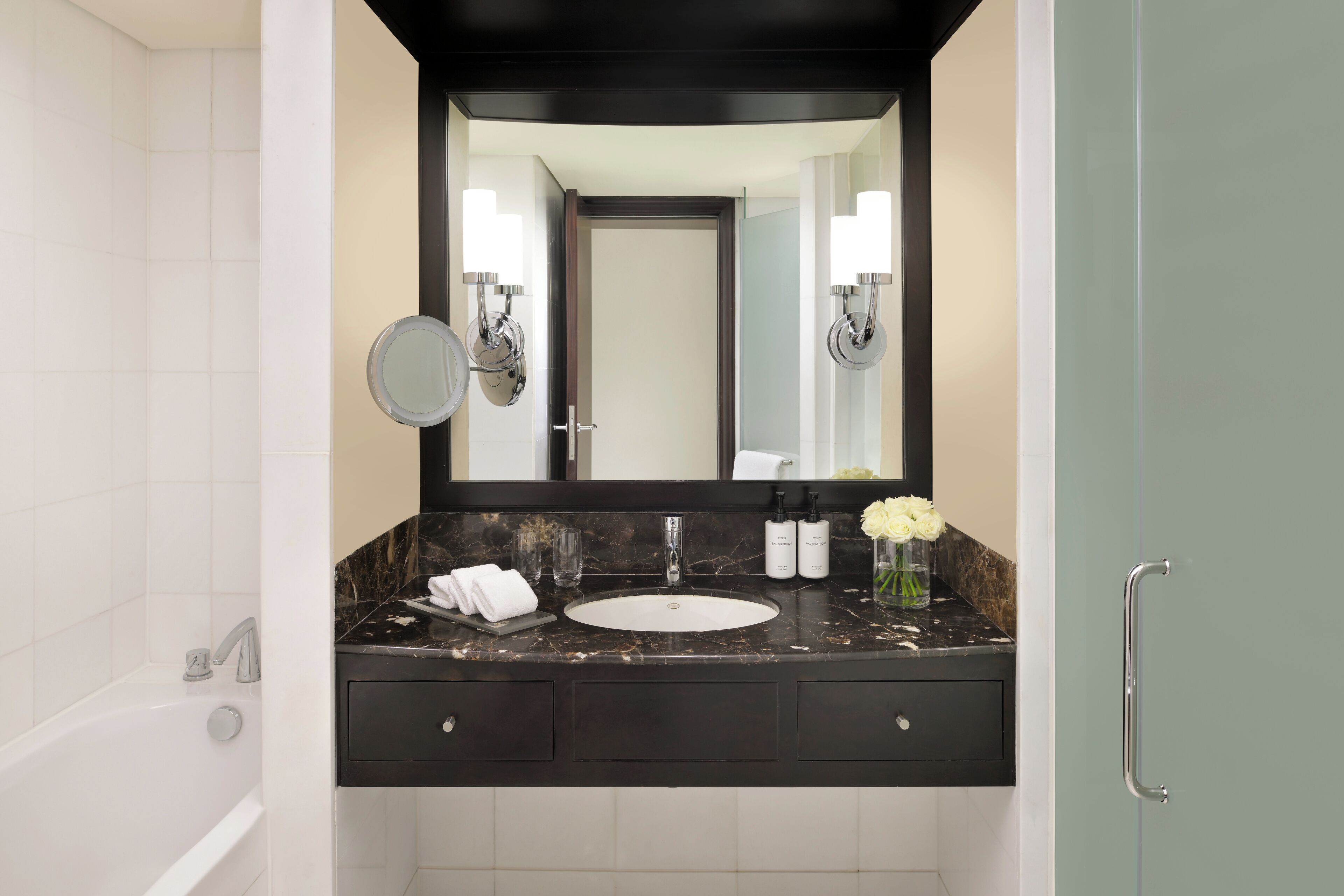 A modern bathroom with a white sink, dark marble countertop, and a large mirror above it.
