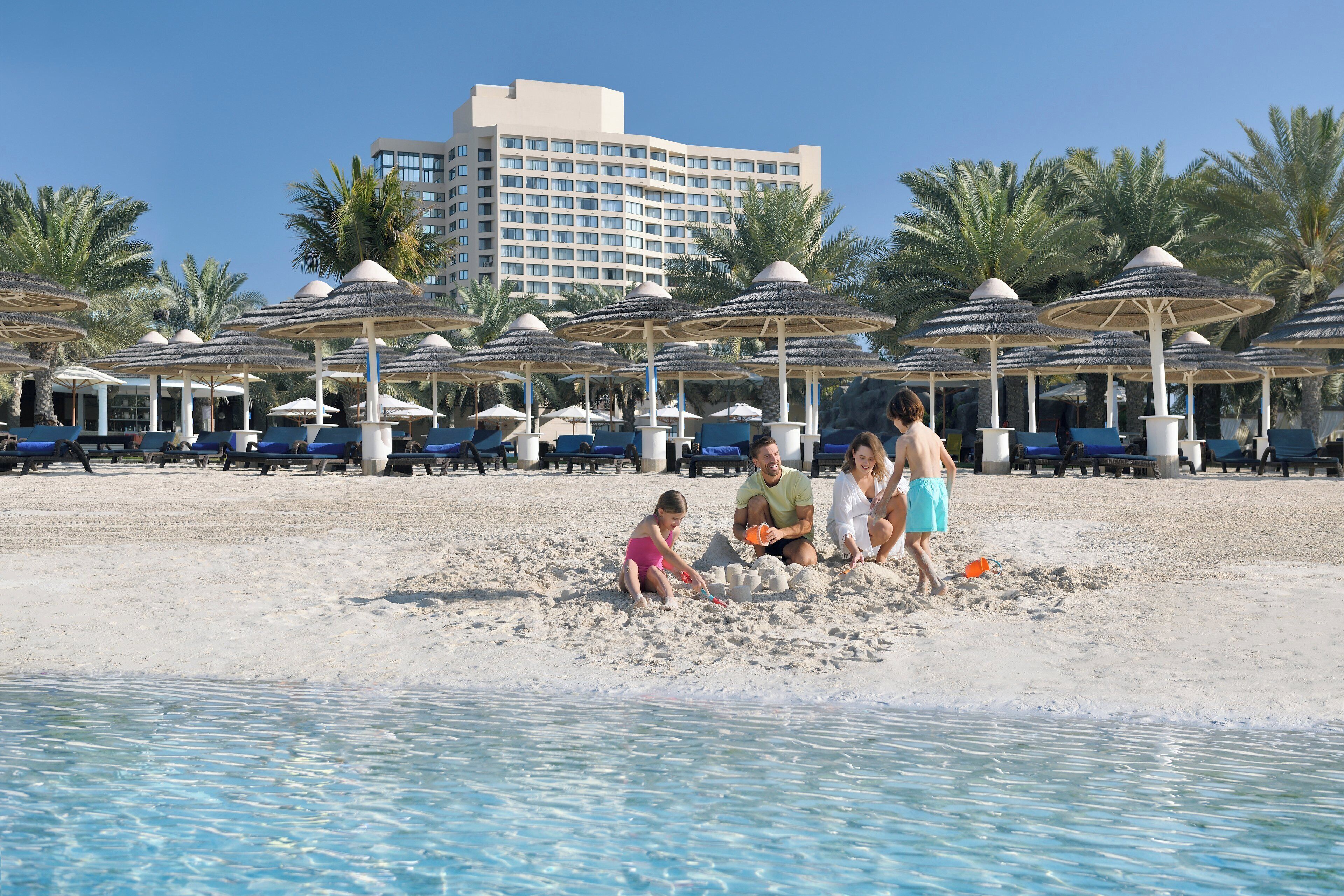 A beach with umbrellas, lounge chairs, and a hotel building in the background.