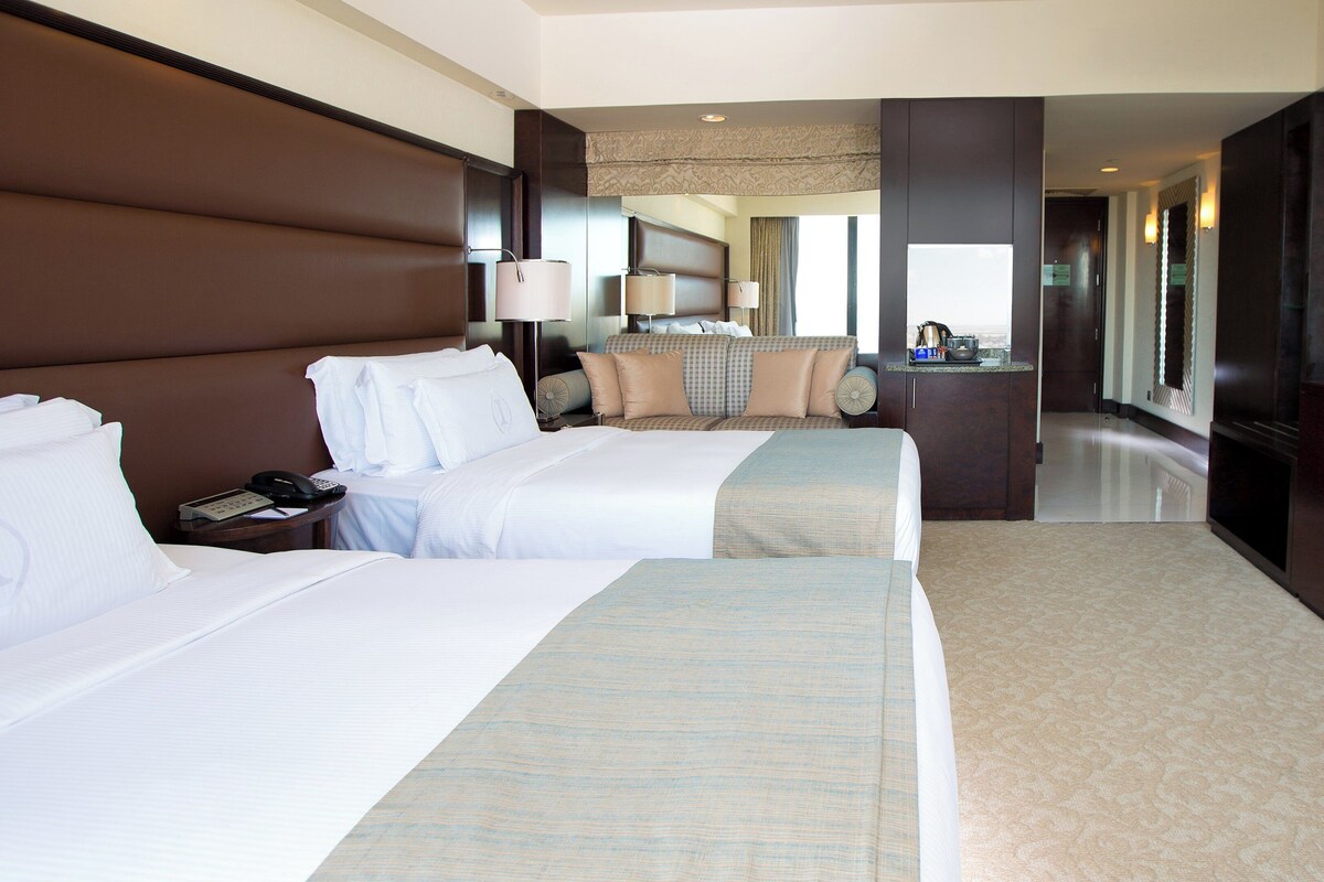 A hotel room with two beds, a desk, a TV, and a bathroom visible through an open door.
