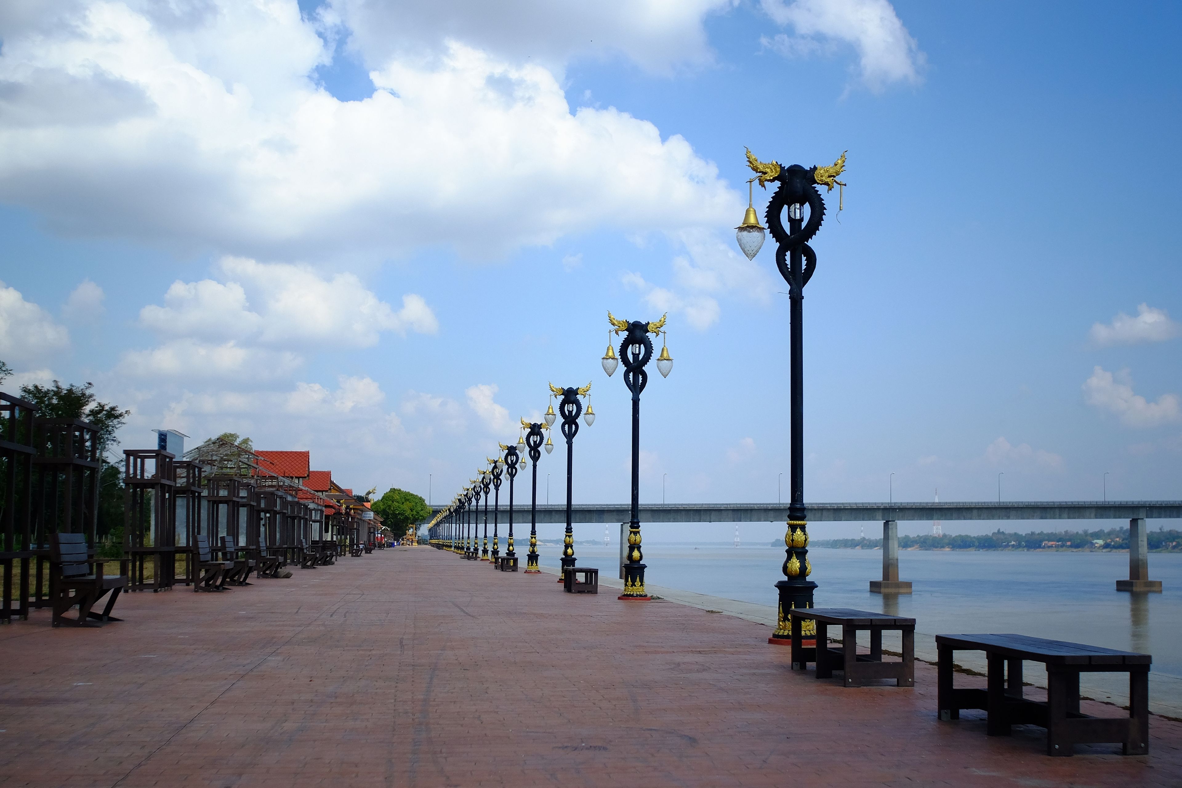 A waterfront promenade with benches and ornate street lamps.