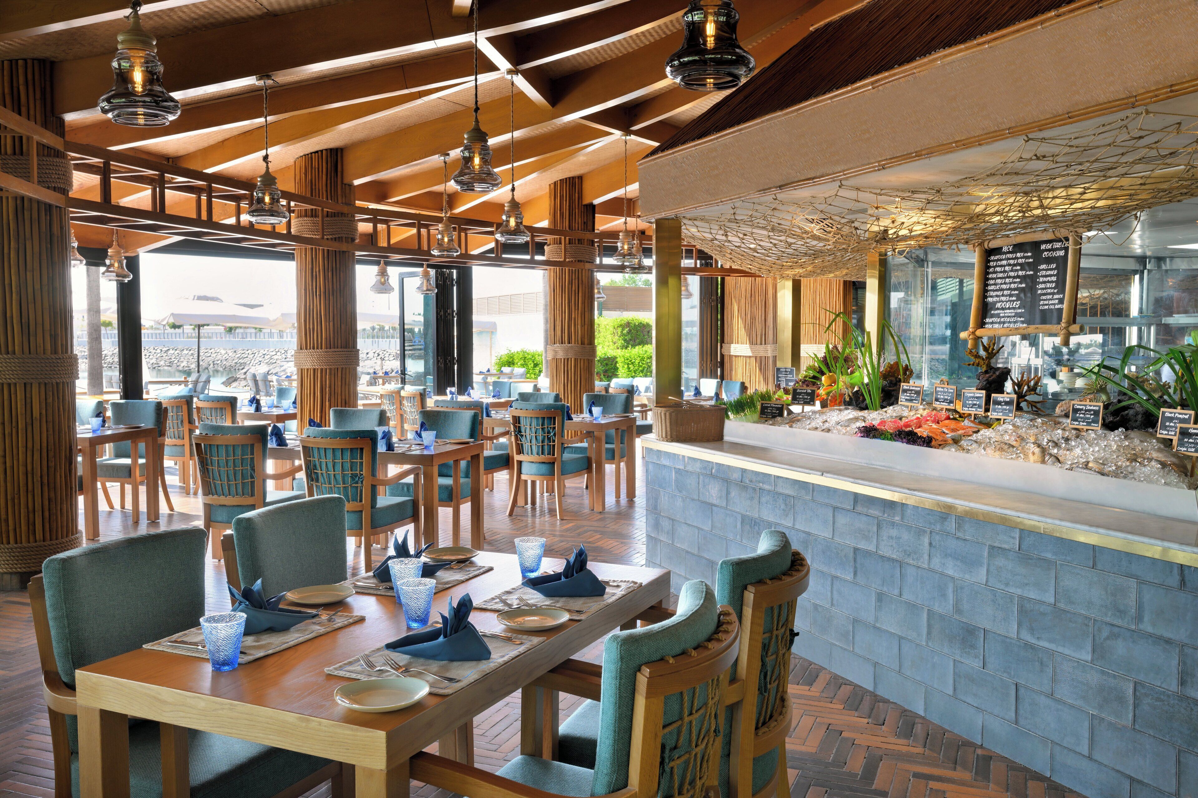 Een restaurant met houten tafels en stoelen, een stenen toonbank en uitzicht op het strand.