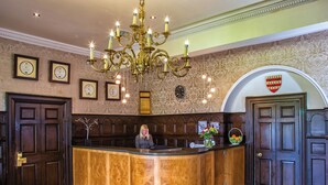 A reception area with a wooden reception desk, a chandelier, framed certificates, and a clock on the wall. - Waterton Park Hotel (Wakefield)