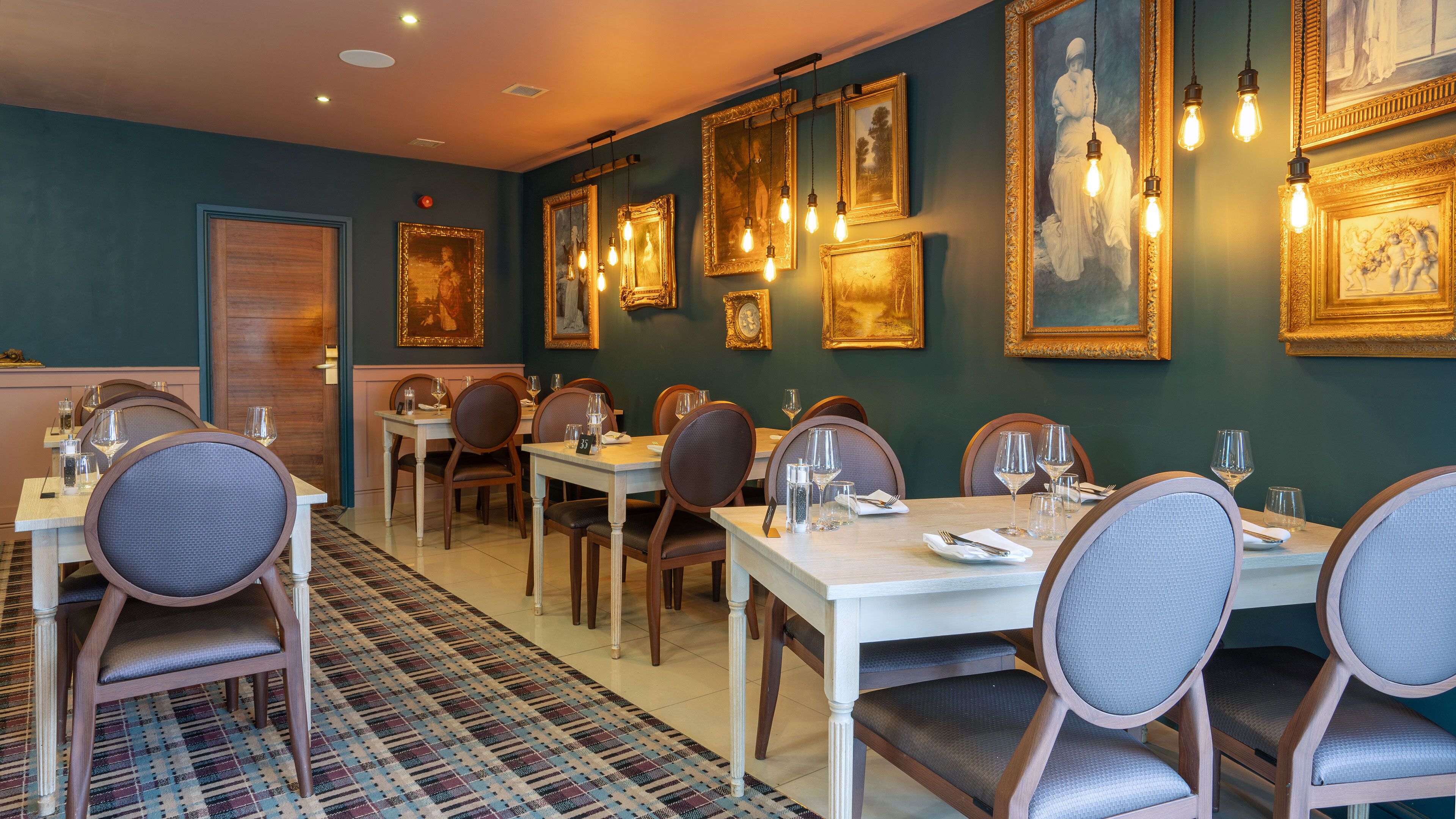 A dining area with tables set for four, chairs, and framed artwork on the walls.