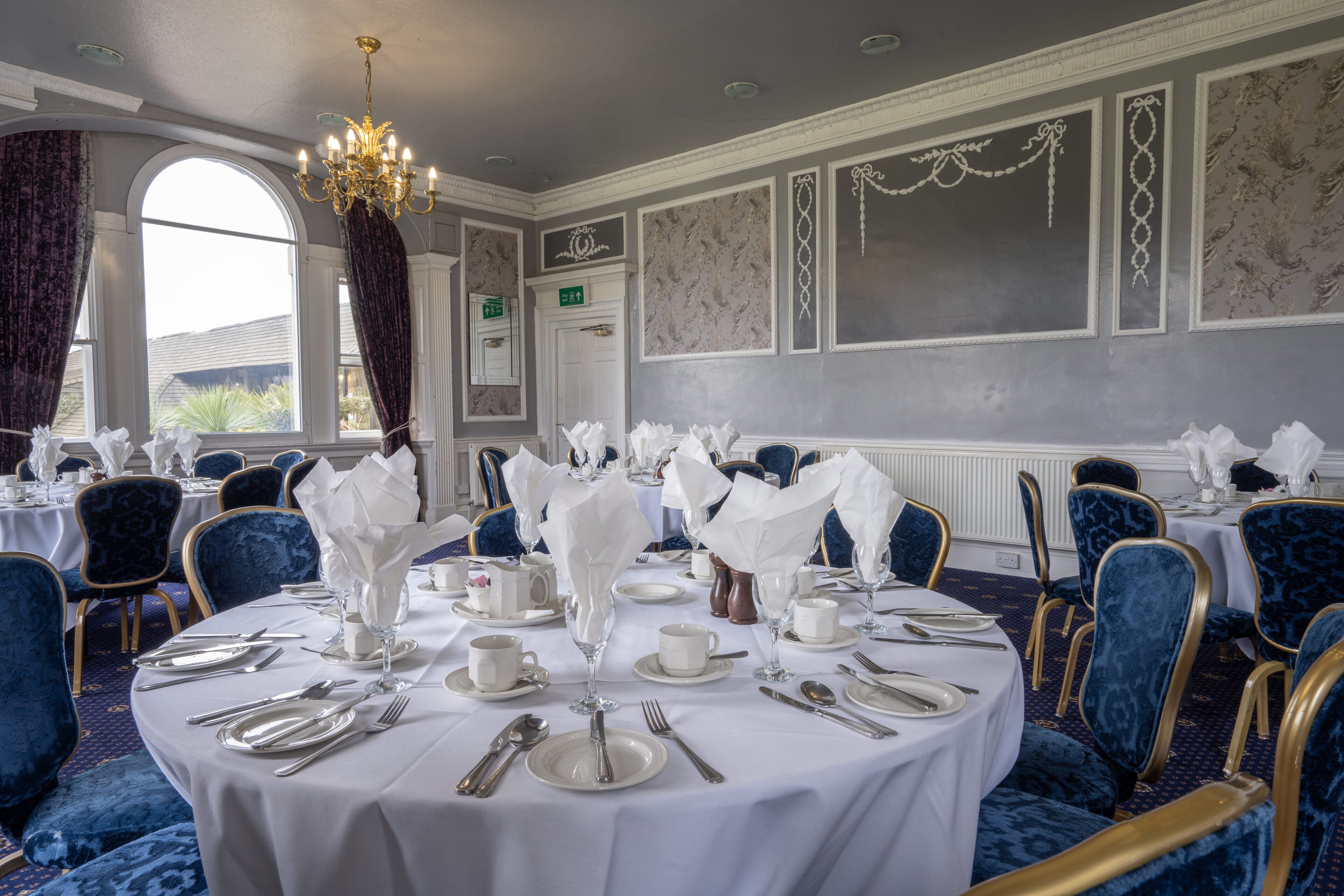 Comedor formal con mesas redondas, sillas tapizadas en azul y vajilla blanca.