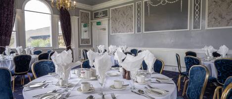 Comedor formal con mesas redondas, sillas tapizadas en azul y vajilla blanca.