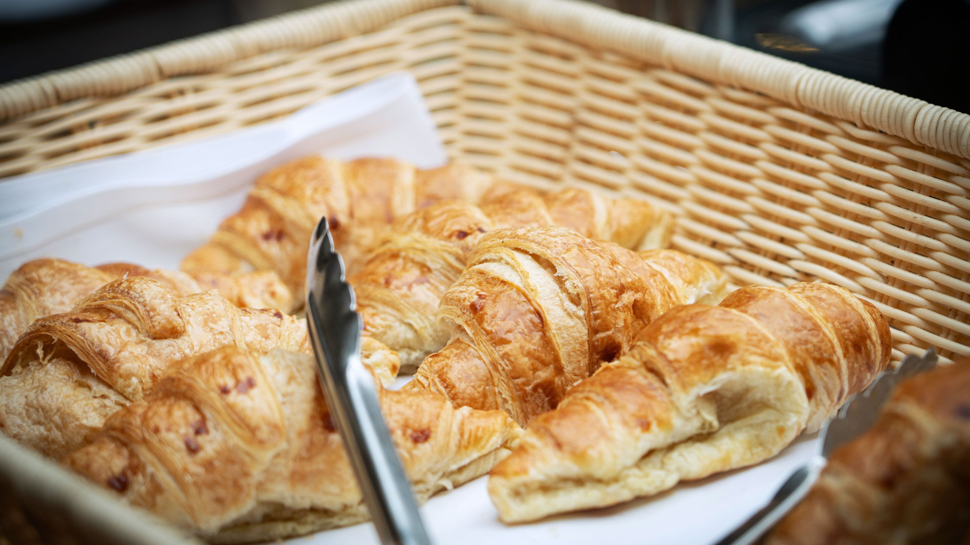 A wicker basket containing croissants and a knife.
