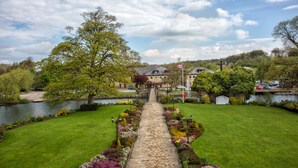 A pathway leading to a building with a flag, surrounded by greenery and a body of water. - Waterton Park Hotel (Wakefield)