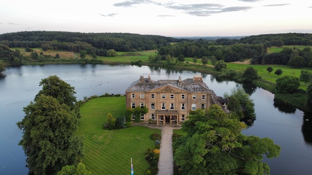 A large, historic building with a symmetrical facade, surrounded by a well-maintained lawn and a body of water. - Waterton Park Hotel (Wakefield)