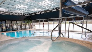An indoor swimming pool with a hot tub, clear glass walls, and a metal roof structure. - Waterton Park Hotel (Wakefield)