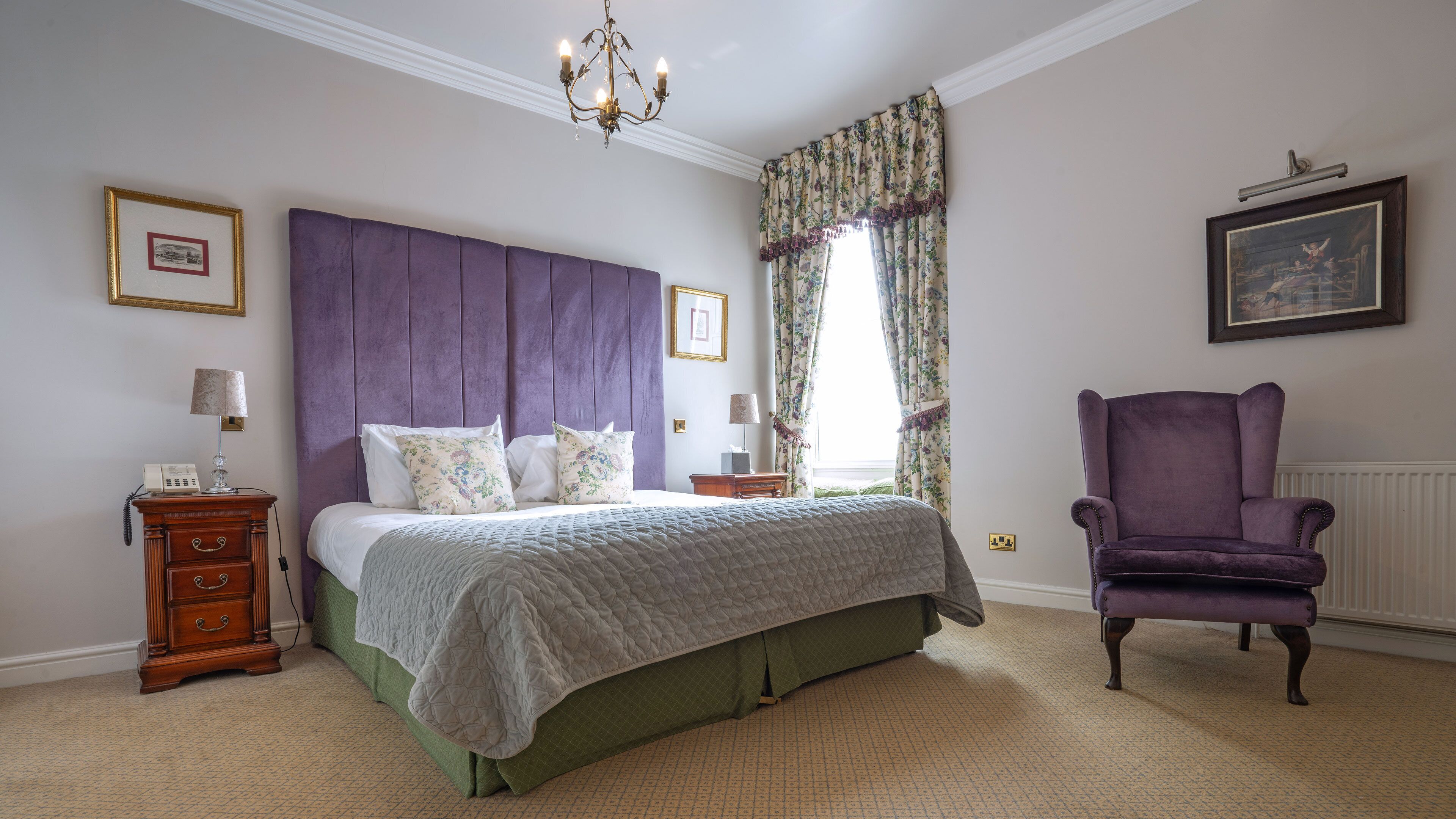 A bedroom with a large bed, a dresser, a chair, and a chandelier.