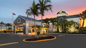 Un hotel con entrada despejada, palmeras y un cielo al atardecer.