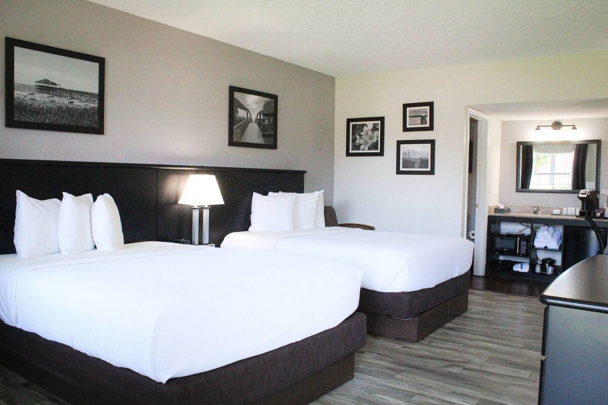 Habitación de hotel con dos camas, una mesita de noche, una lámpara, un aparador y un espejo.