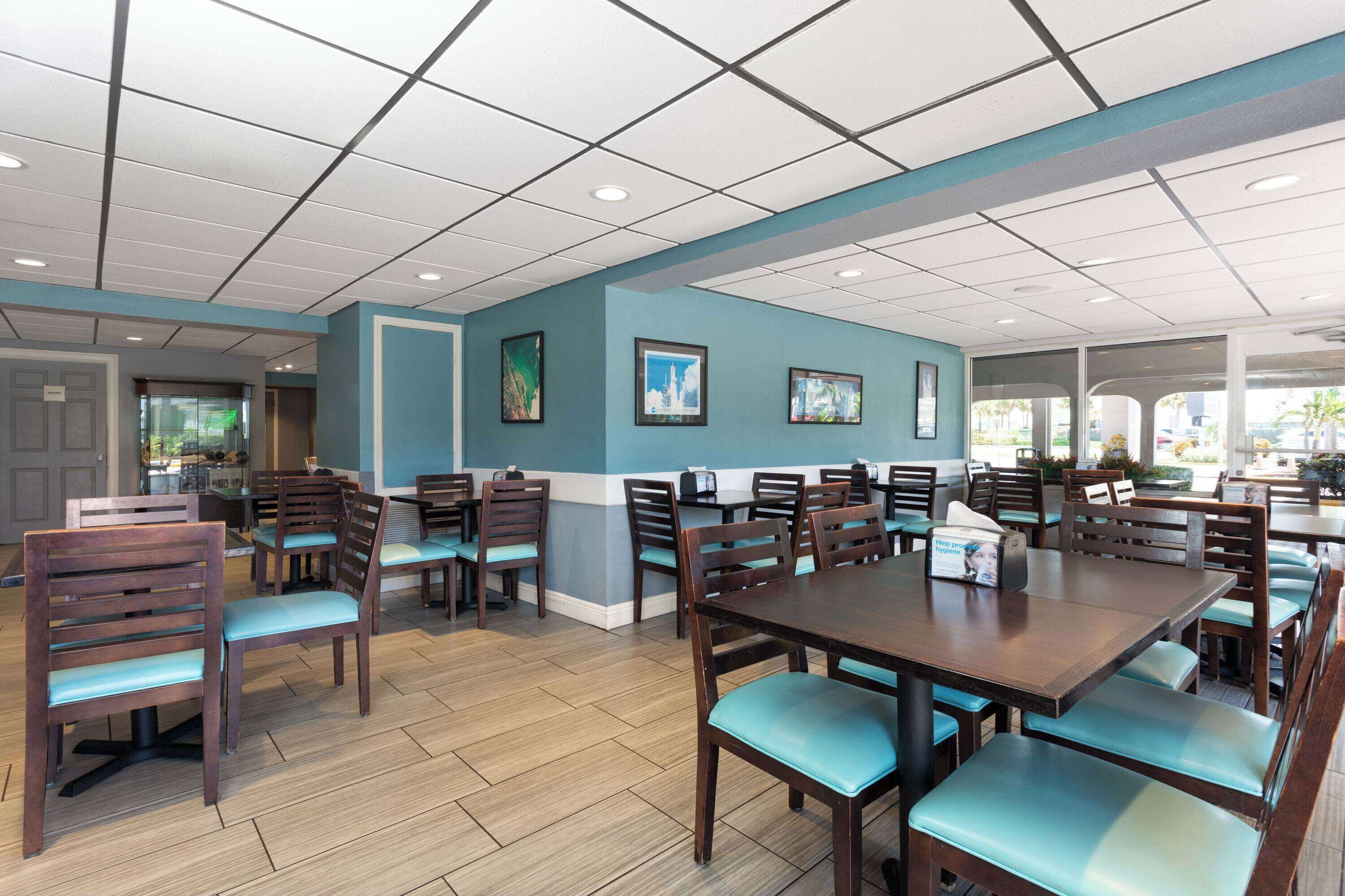 A spacious dining area with wooden tables and chairs, a tiled ceiling, and framed artwork on the walls.