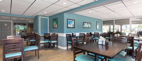 A spacious dining area with wooden tables and chairs, a tiled ceiling, and framed artwork on the walls.
