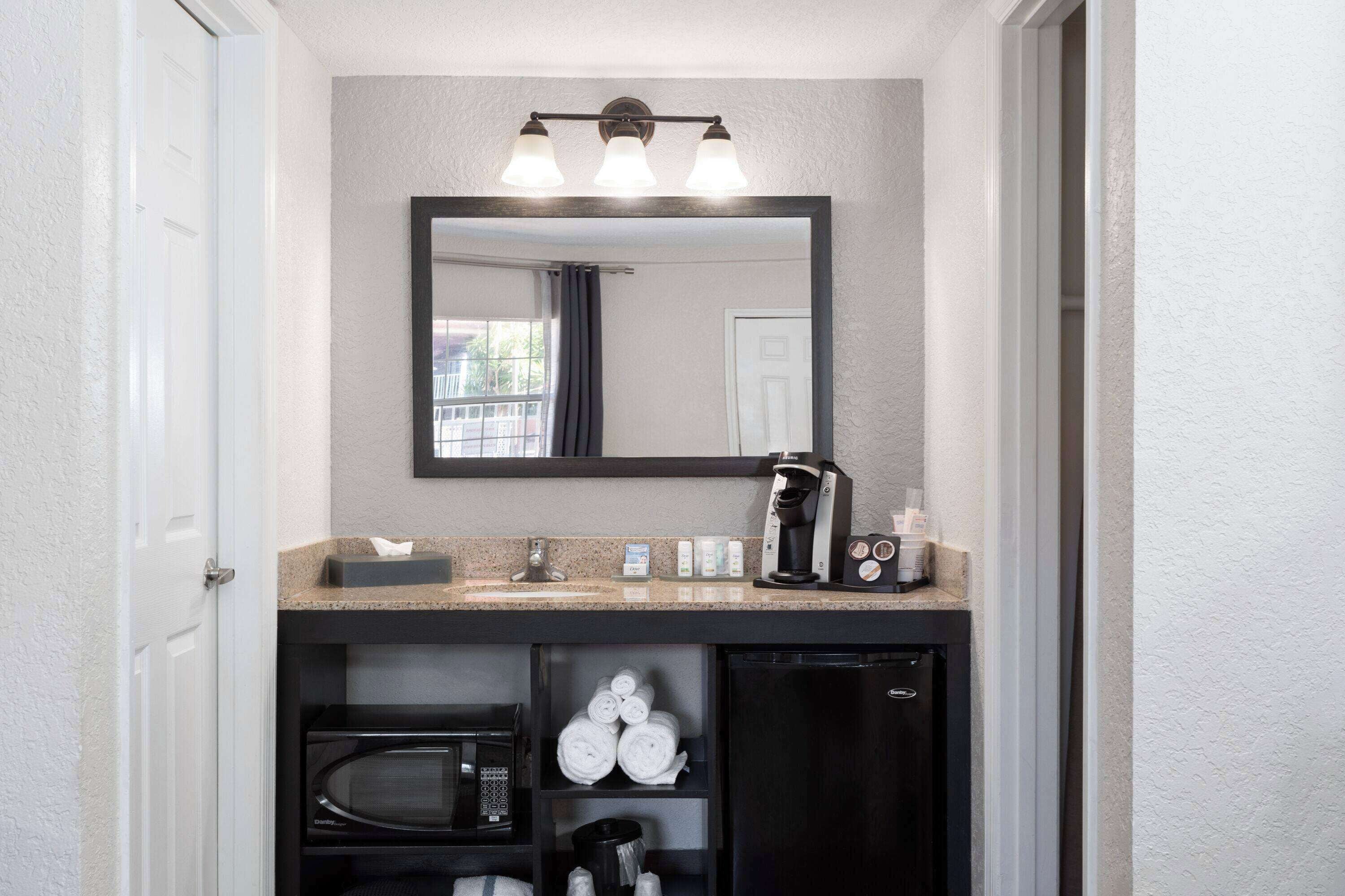 A compact bathroom with a sink, mirror, and a coffee maker.