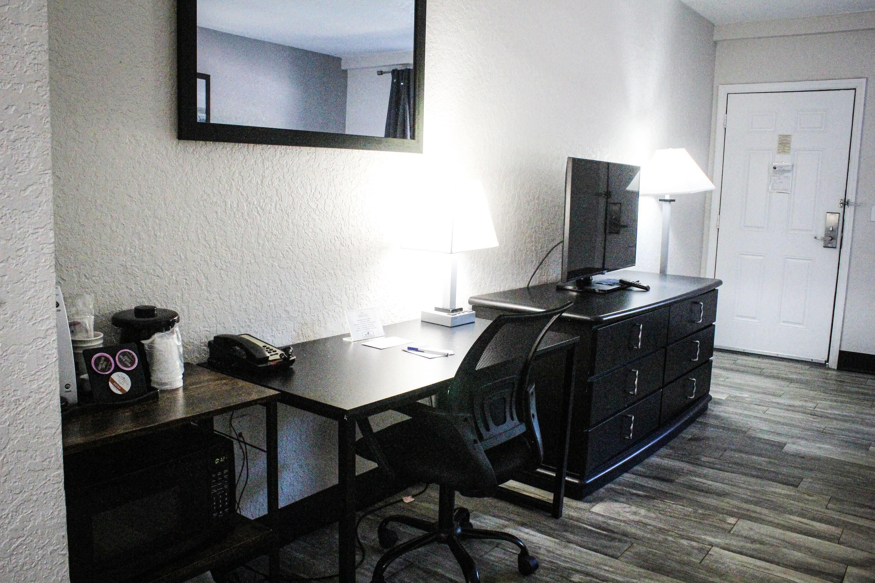 A hotel room with a desk, chair, television, lamp, and a door.