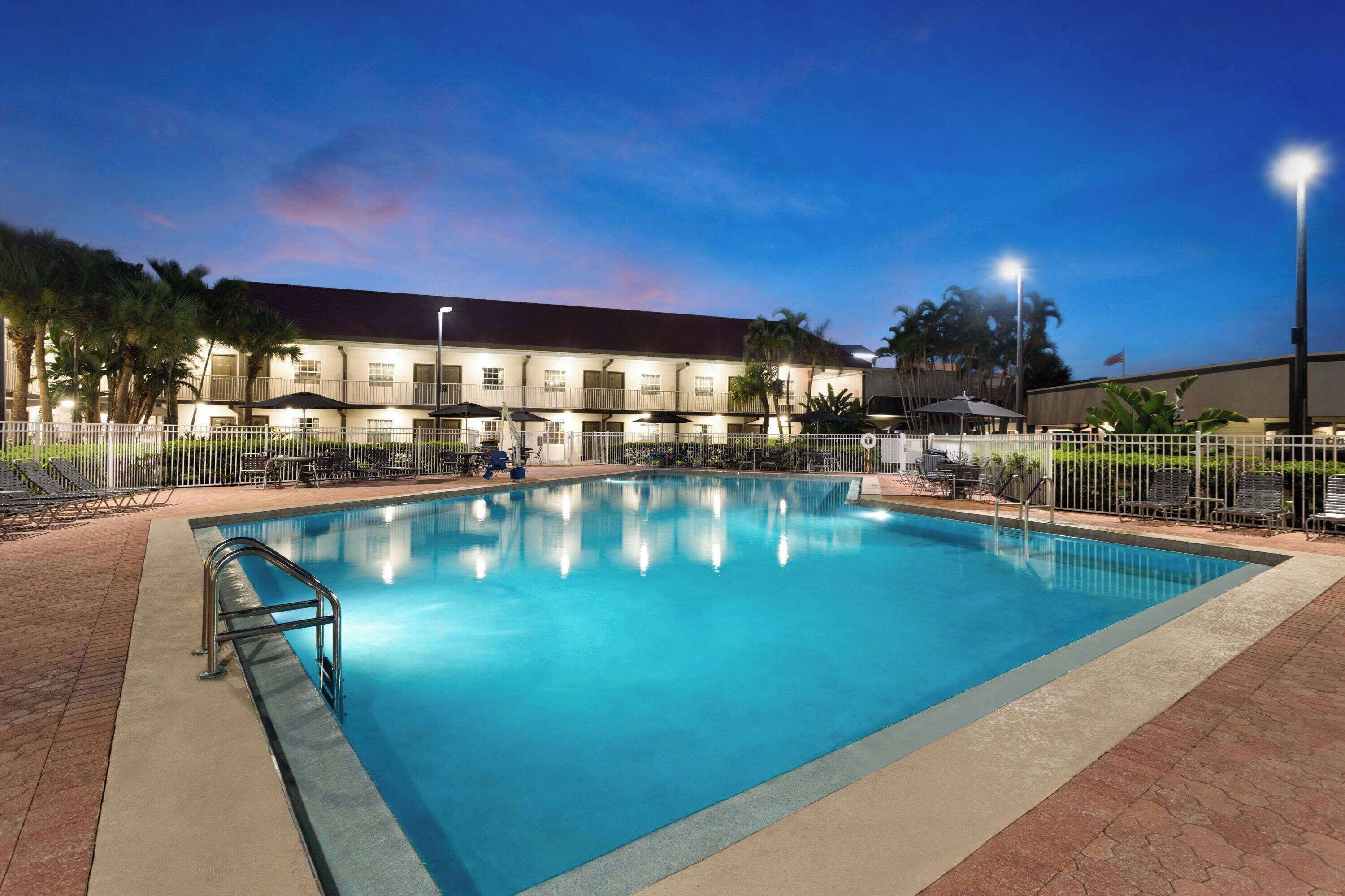 A swimming pool with a metal railing, surrounded by lounge chairs and umbrellas, with a building in the background.