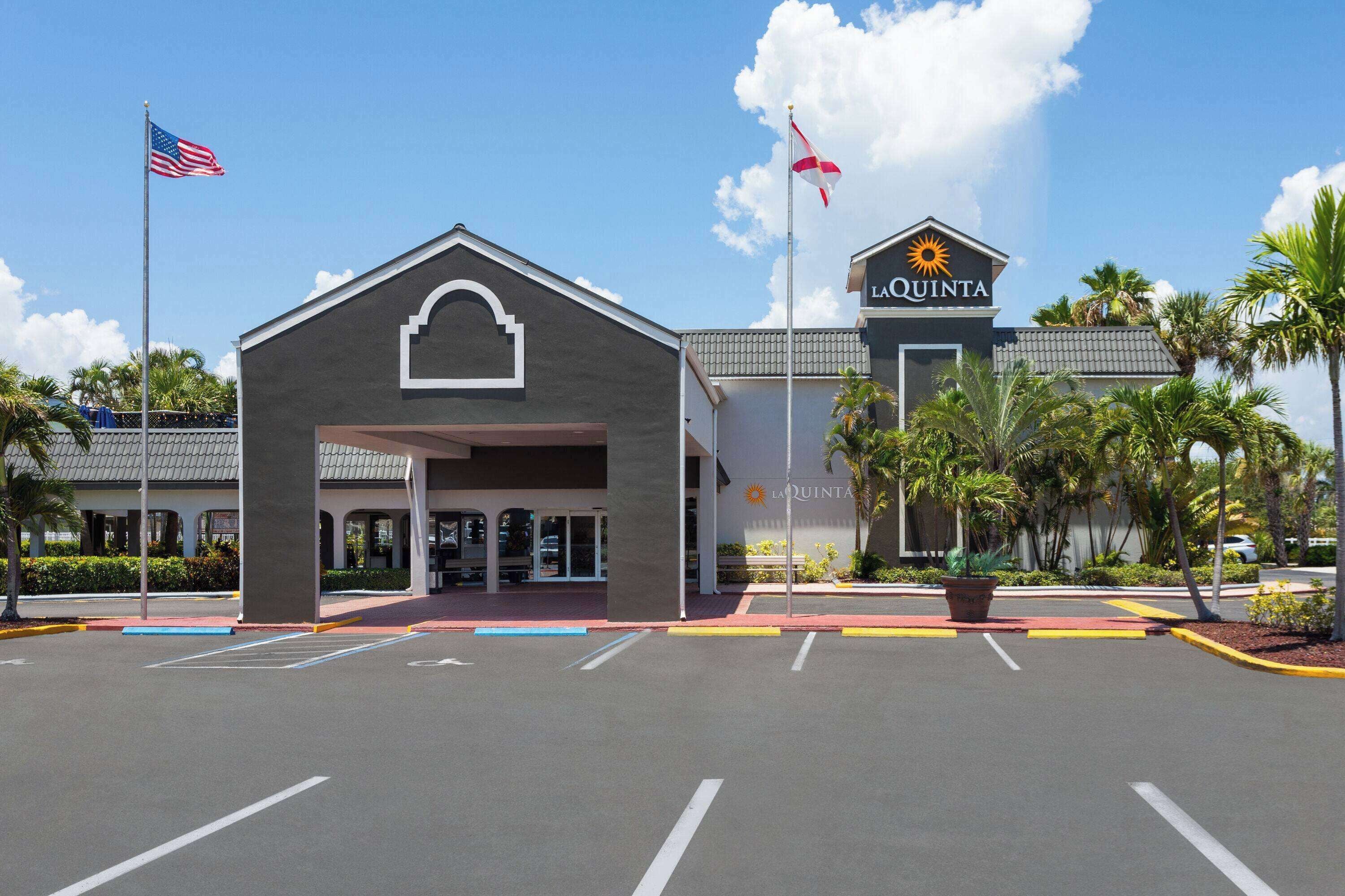 A hotel entrance with a La Quinta sign, American and another flag, and a parking lot with marked spaces.