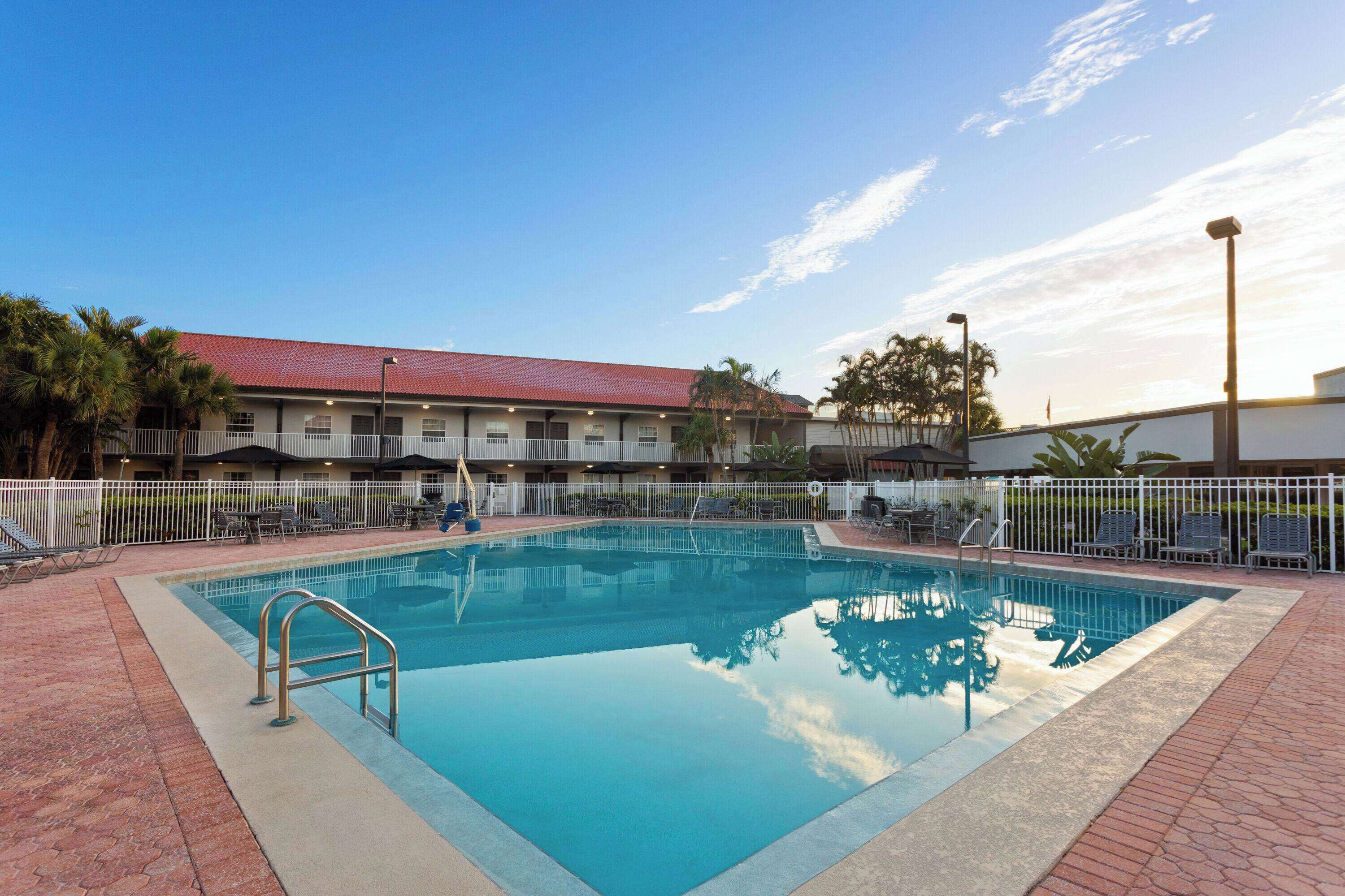 A swimming pool with a metal ladder, surrounded by a white fence and lounge chairs.