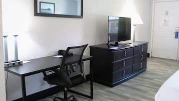 A hotel room with a desk, chair, television, dresser, and a door.