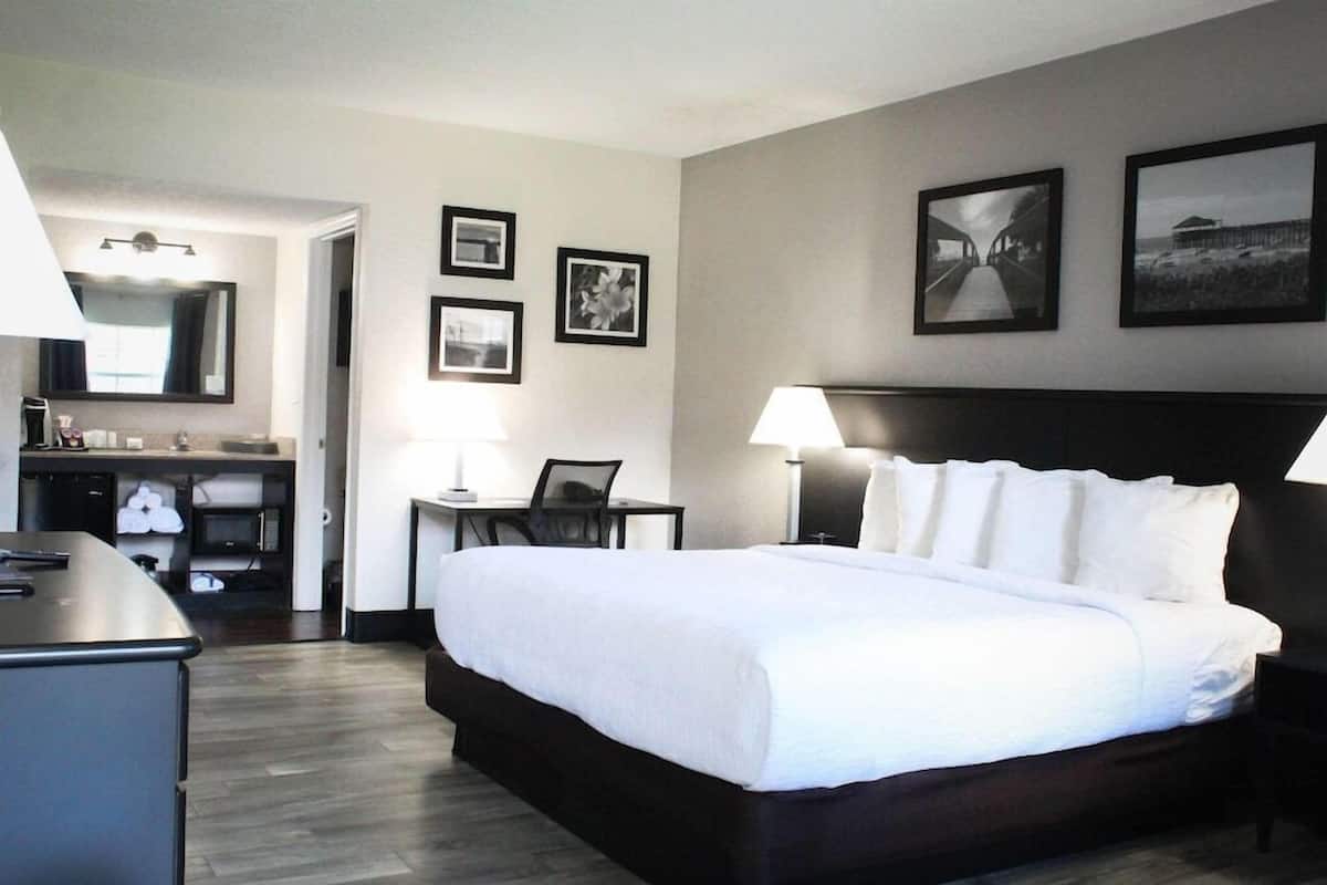 Habitación de hotel con una cama grande, un escritorio, una silla, un espejo y cuadros en la pared.