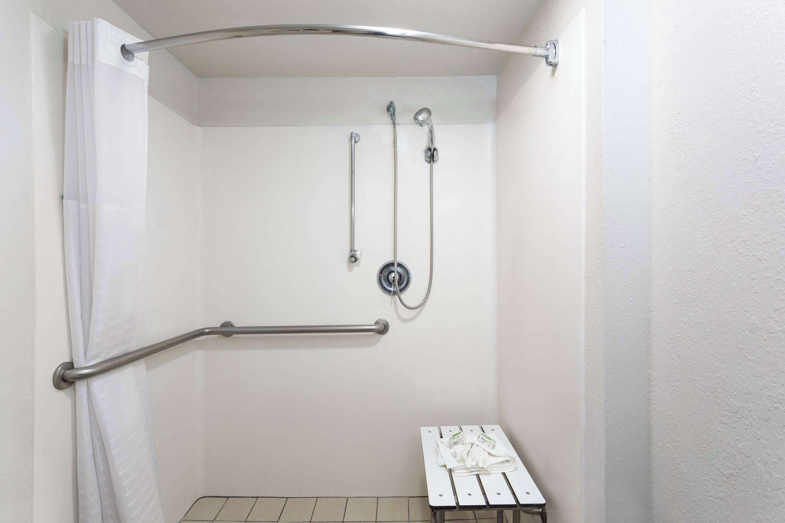 A shower with a grab bar, a handheld showerhead, and a wall-mounted faucet.