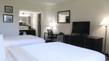 Habitación de hotel con dos camas, un escritorio con silla, televisión, espejo y lámpara.
