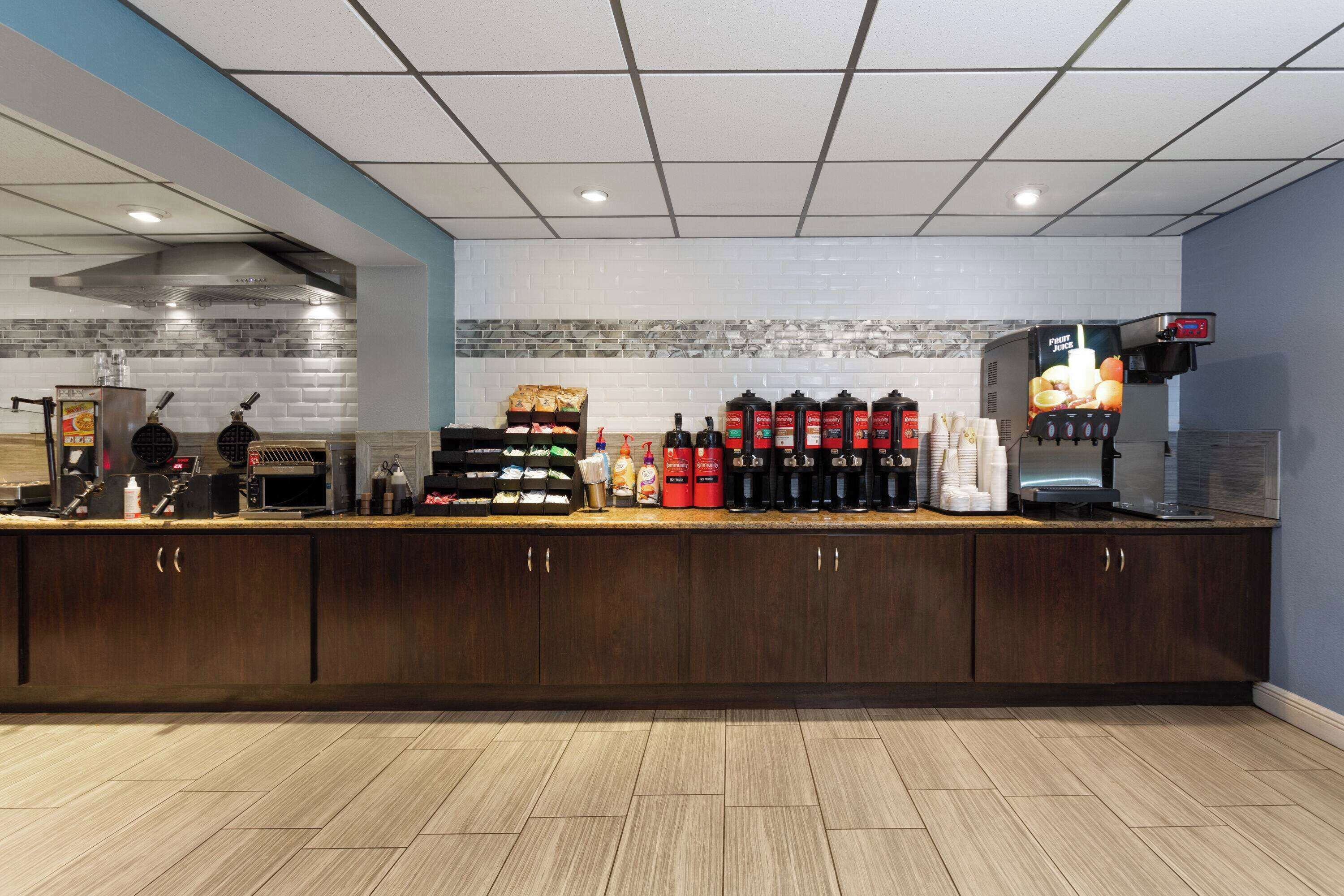 A modern kitchen area with a coffee station, including a coffee machine, various coffee dispensers, and a fruit juice dispenser.