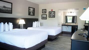 A hotel room with two beds, a desk, a mirror, and a lamp.