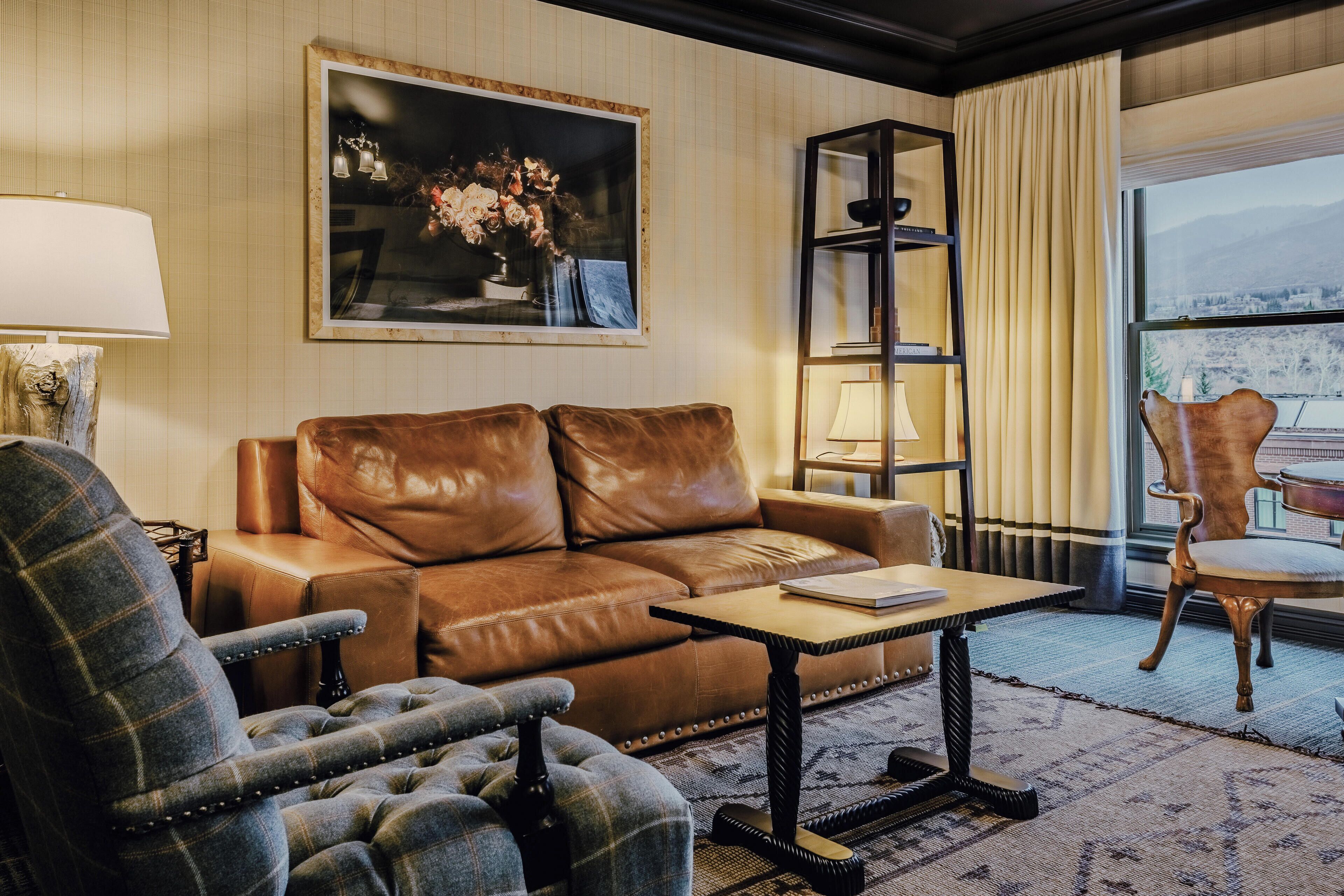 A living room with a brown leather sofa, a plaid armchair, a small table, and a bookshelf.