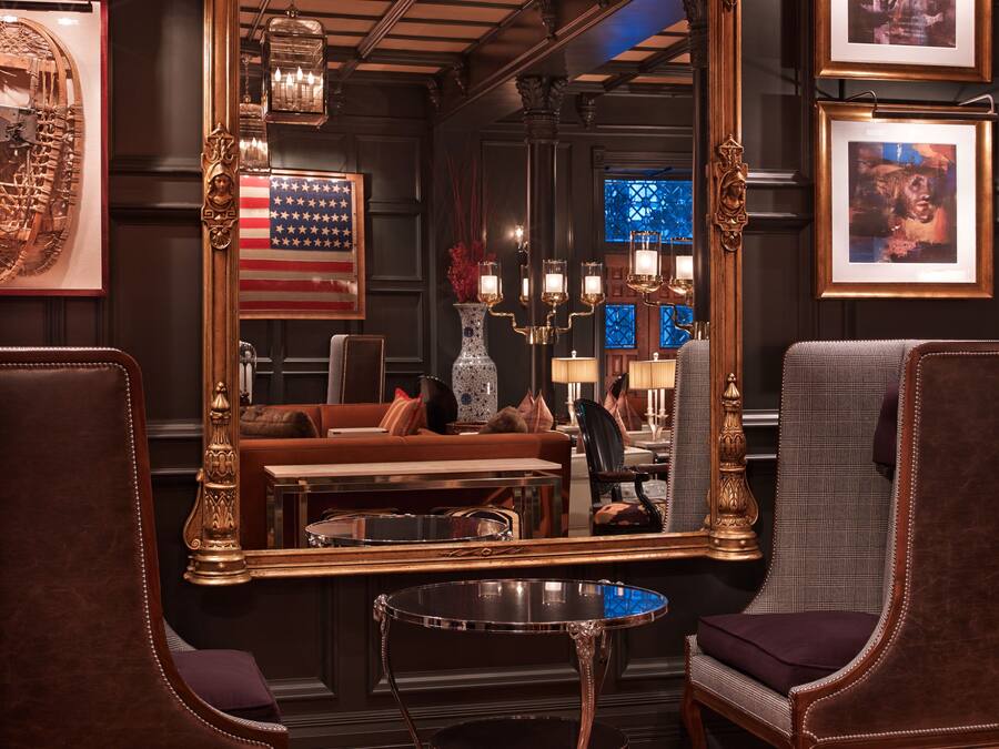 Ein luxuriöses Zimmer mit einem großen Spiegel, der das Interieur widergibt, einer Couch, einem Couchtisch und einem Essbereich mit einem Kronleuchter.