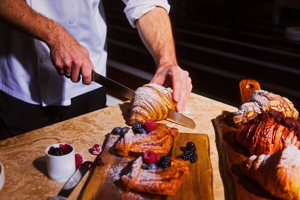 Uma pessoa cortando um pastel em uma tábua de madeira, com outros pastéis e frutas vermelhas ao redor.