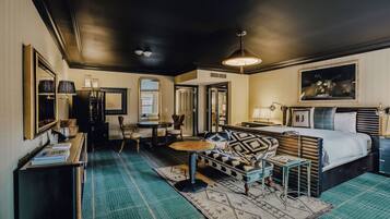 Habitación de hotel con cama, sofá, escritorio y silla. Se ve una ventana y una puerta.