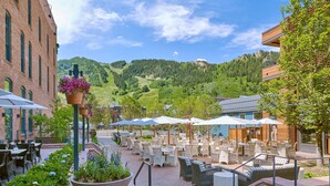 An outdoor patio with tables and chairs, surrounded by greenery and a mountain view.