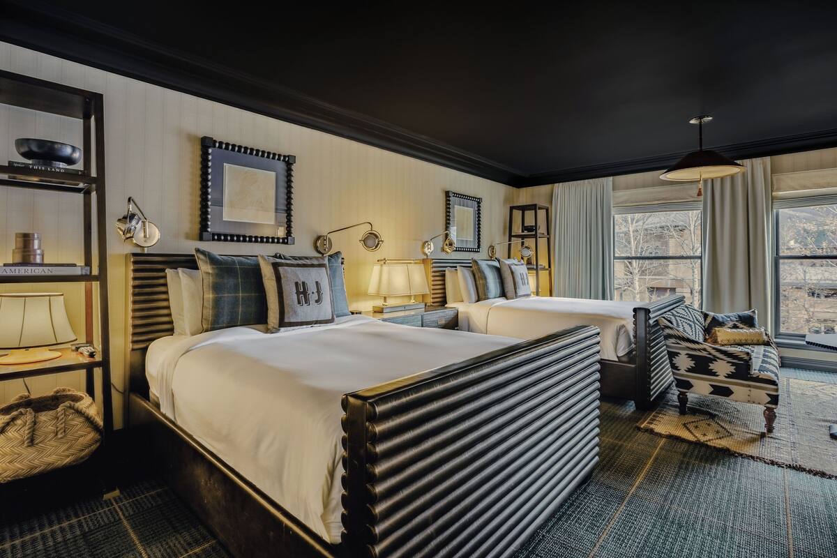 Une chambre d’hôtel avec deux lits, un canapé, un bureau avec une lampe et une vue sur l’extérieur.
